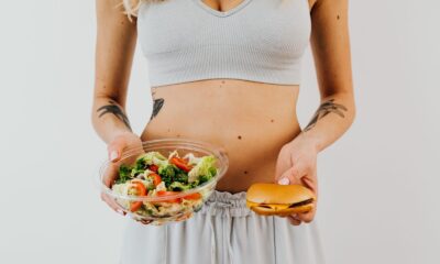 A woman in a sports bra holding a salad and cheeseburger, representing healthy vs junk food choices.