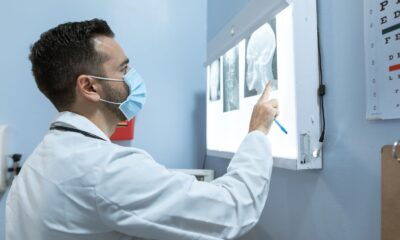 A healthcare professional examines brain X-rays while wearing a face mask in a hospital setting.