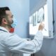 A healthcare professional examines brain X-rays while wearing a face mask in a hospital setting.