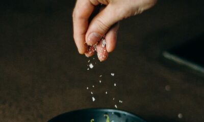 A hand sprinkles salt over a bowl of fresh edamame beans, capturing a moment of delicious meal preparation.