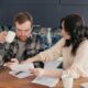 A couple reviews household bills in a kitchen, appearing concerned and focused.