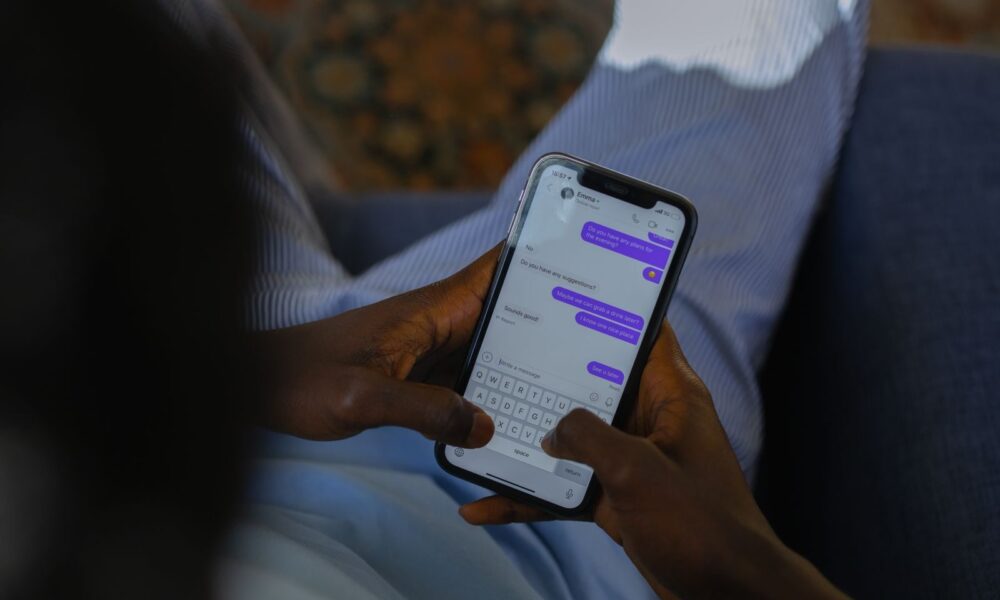 Close-up of hands holding a smartphone, typing a message on a touch screen indoors.