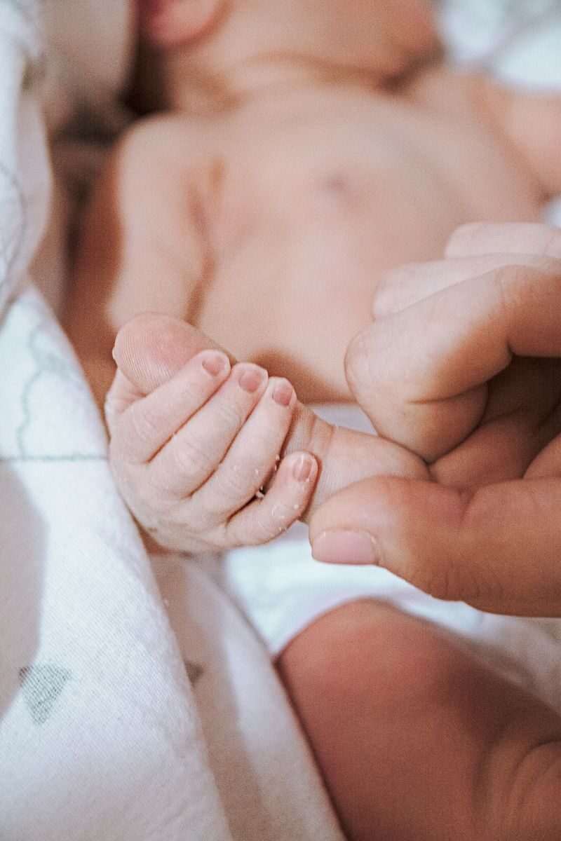A newborn baby gently holds an adult's finger, symbolizing love and connection.