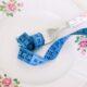 A floral plate with a fork and blue measuring tape symbolizing dieting or healthy eating.
