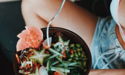 From above of crop anonymous young woman in summer clothes sitting with crossed legs and enjoying healthy salad bowl