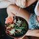 From above of crop anonymous young woman in summer clothes sitting with crossed legs and enjoying healthy salad bowl