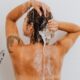 Rear view of a woman washing her hair in the shower, showcasing a tattoo and emphasizing hygiene.