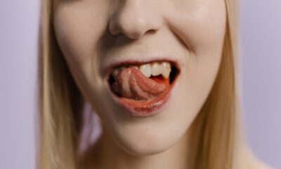Close-up portrait of a blonde woman with her tongue out against a neutral background.