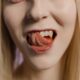 Close-up portrait of a blonde woman with her tongue out against a neutral background.