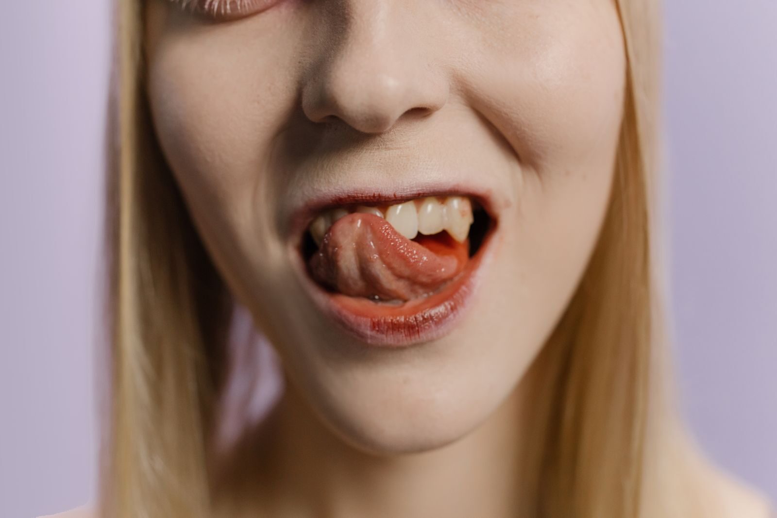 Close-up portrait of a blonde woman with her tongue out against a neutral background.