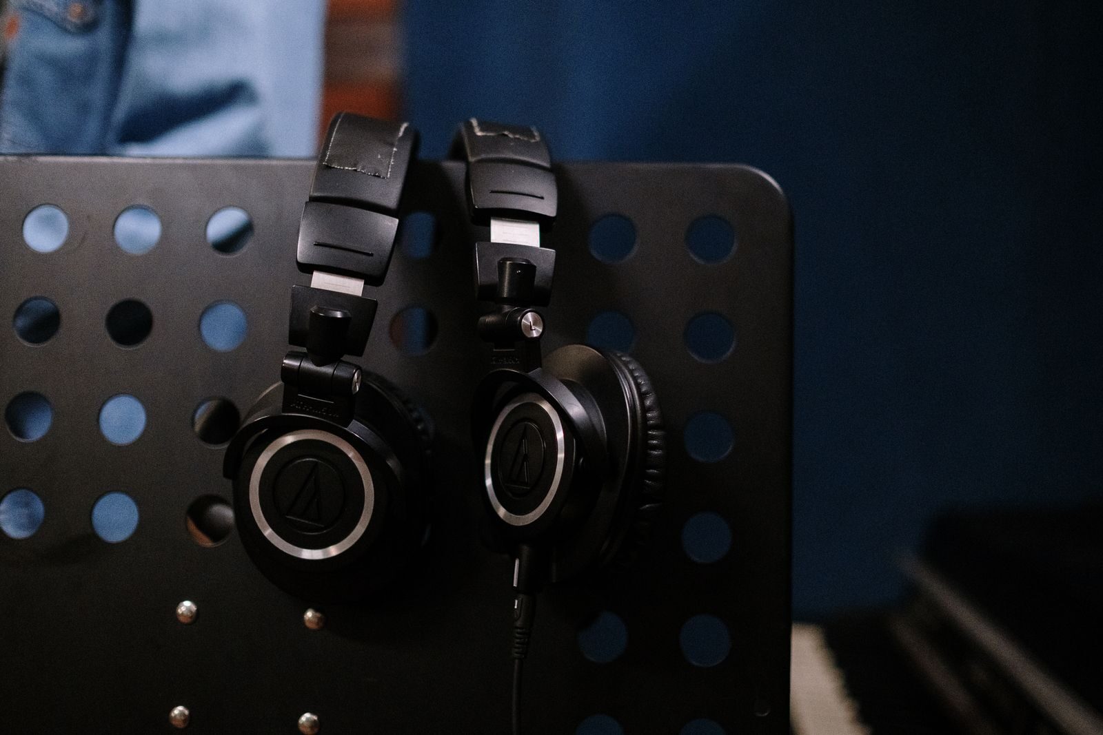 Close-up of professional headphones hanging on a perforated music stand in a studio setting.