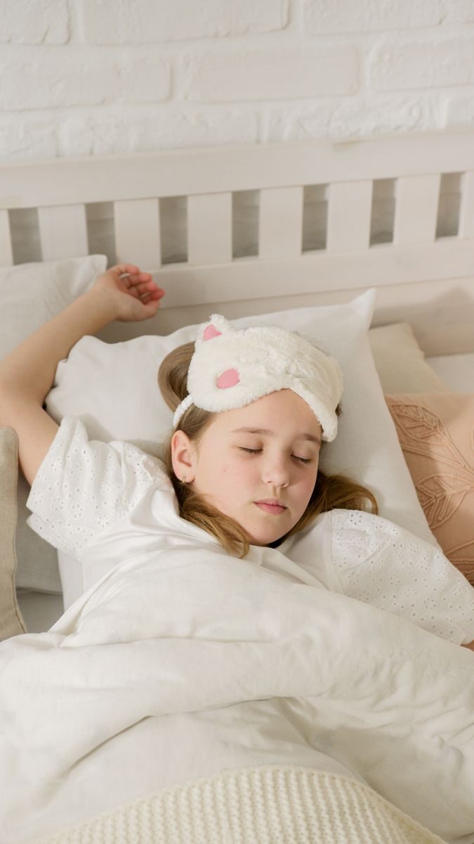 A young girl peacefully sleeping in bed with a soft eye mask, embodying comfort and innocence.