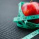 A vibrant red apple encircled by a blue measuring tape, symbolizing health and weight management.