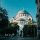 View of the iconic Saint Sava Temple in Belgrade on a sunny day, framed by trees and buildings.