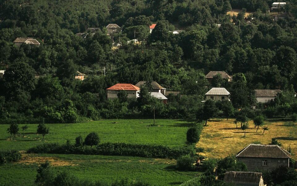 A picturesque village nestled among verdant hills and dense forests, showcasing rural beauty.