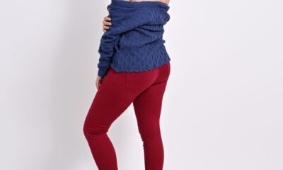 Stylish woman in blue sweater and red pants posing on a white background.