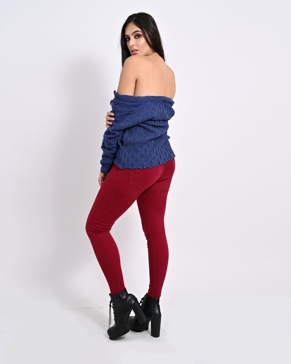 Stylish woman in blue sweater and red pants posing on a white background.