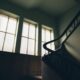 Dimly lit vintage staircase with iron handrail and large windows, creating a nostalgic atmosphere.