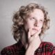 Portrait of a young adult with curly blond hair, deep in thought indoors.
