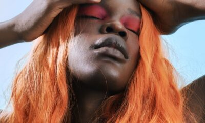 Striking portrait of a person with vibrant orange hair and bold pink eye makeup, eyes closed.