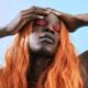 Striking portrait of a person with vibrant orange hair and bold pink eye makeup, eyes closed.