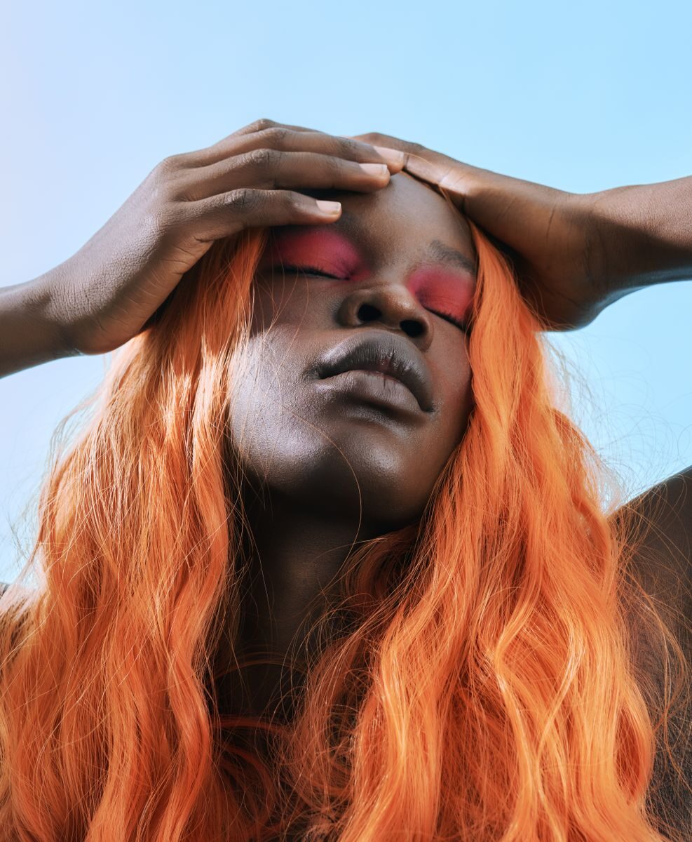 Striking portrait of a person with vibrant orange hair and bold pink eye makeup, eyes closed.