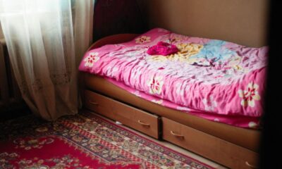 A warm and inviting bedroom scene featuring a floral pink bedspread, under-bed drawers, and a patterned rug.