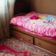 A warm and inviting bedroom scene featuring a floral pink bedspread, under-bed drawers, and a patterned rug.