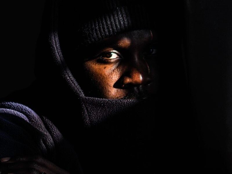 Moody portrait of a man in low light wearing a hooded jacket.