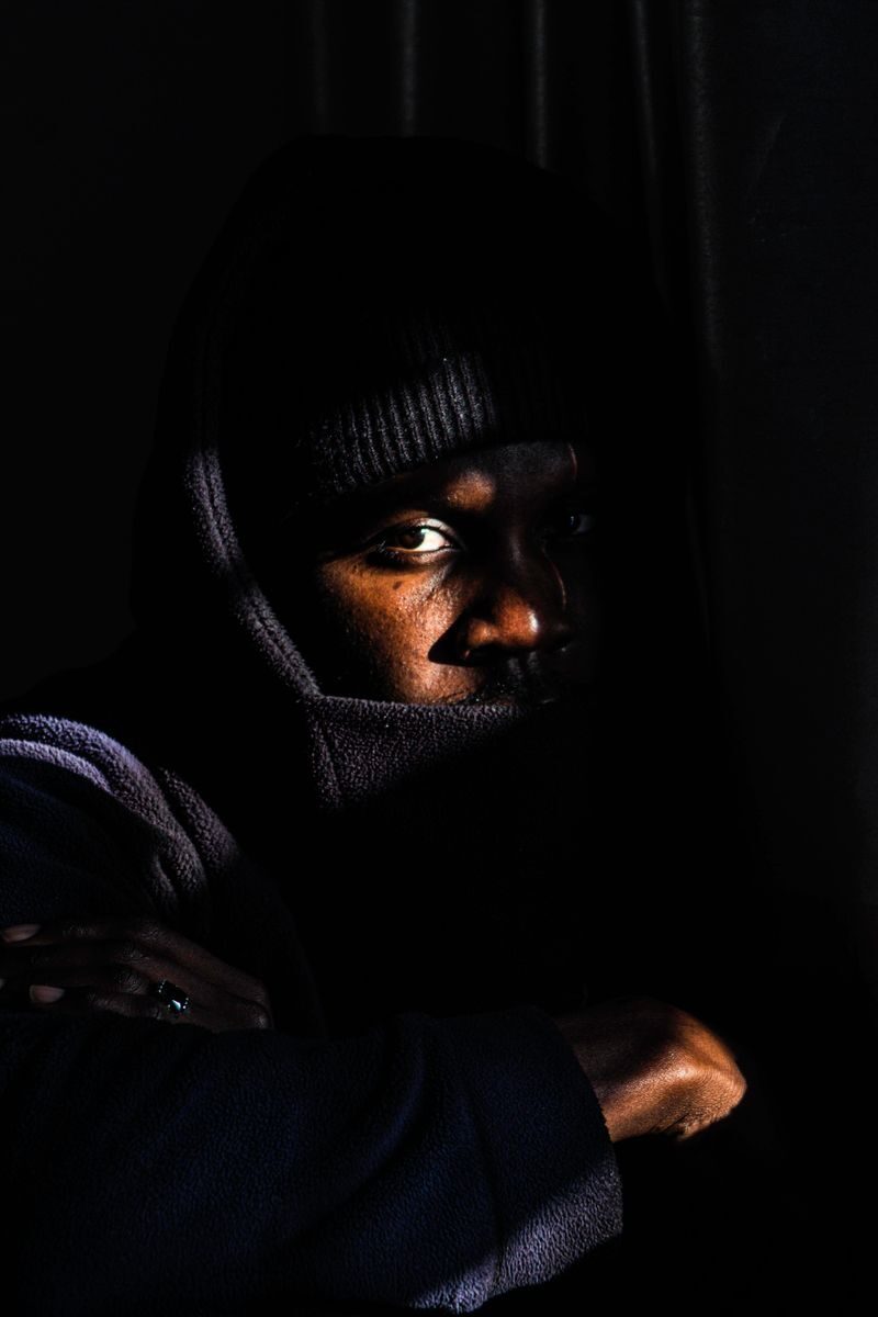 Moody portrait of a man in low light wearing a hooded jacket.