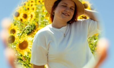 A woman enjoys a sunny day with sunflowers, reflected in a mirror.