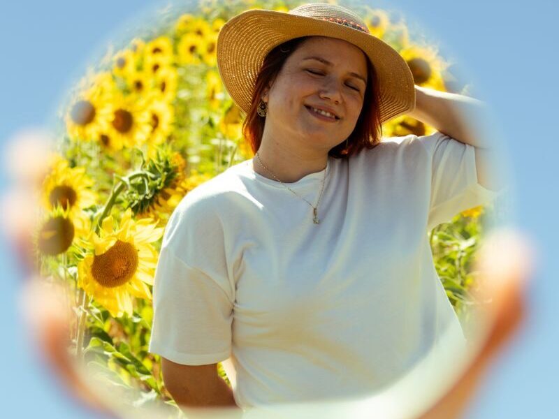 A woman enjoys a sunny day with sunflowers, reflected in a mirror.
