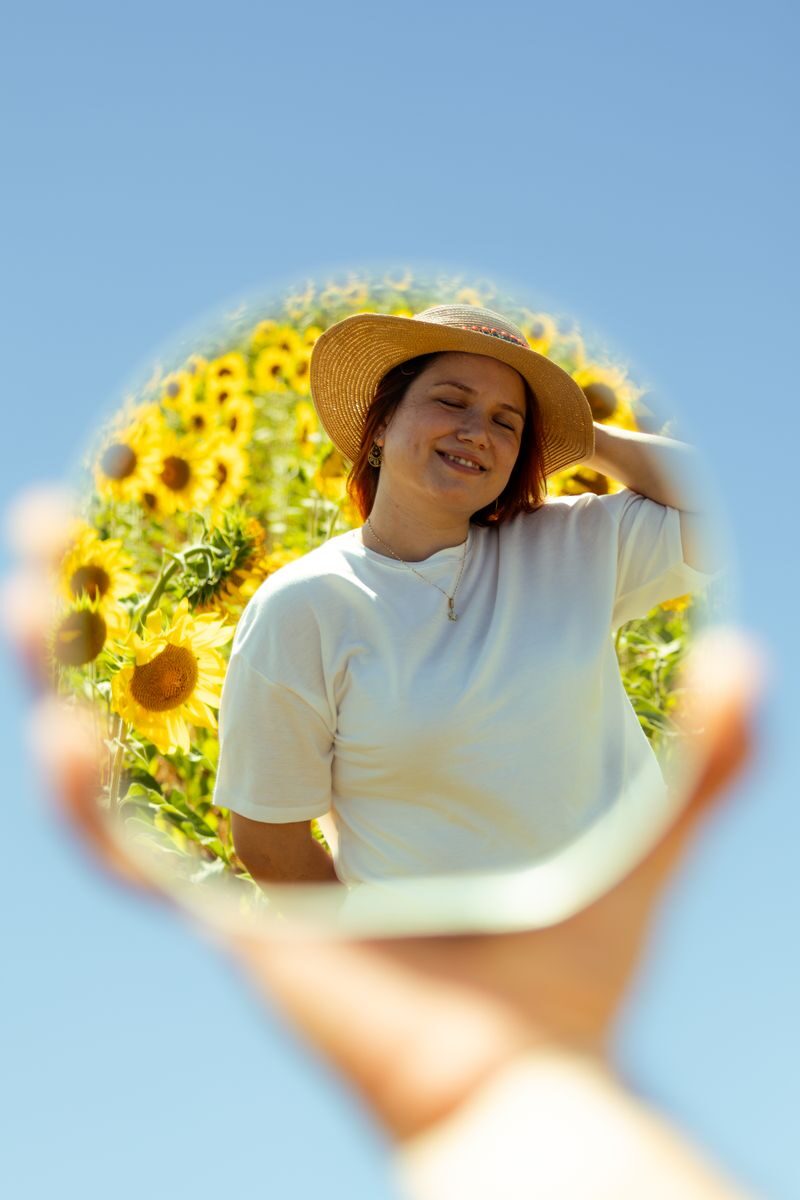 A woman enjoys a sunny day with sunflowers, reflected in a mirror.