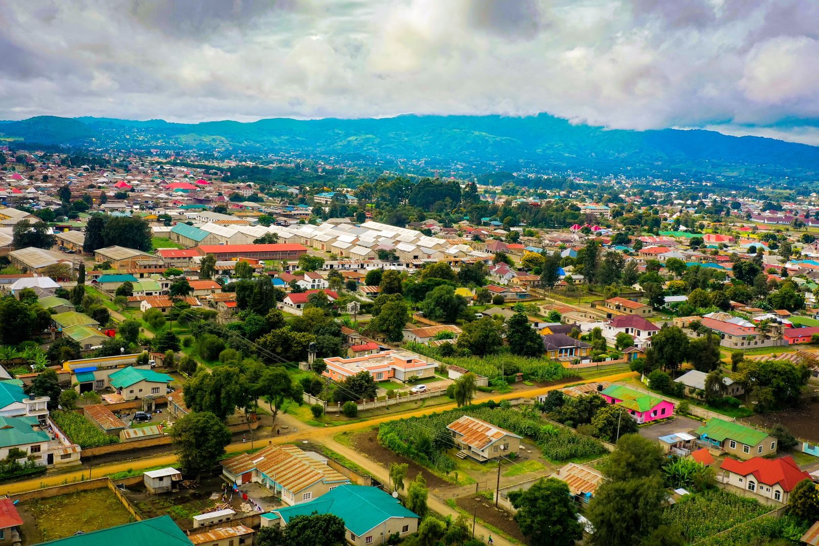 Drone shot of a vibrant townscape in Mbeya, Tanzania, surrounded by greenery and hills.