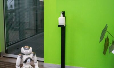 A robot stands near a sanitizer dispenser inside the Goethe Institut with a green wall backdrop.