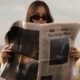 A woman outdoors reading The New York Times wearing sunglasses, with a stylish vibe.