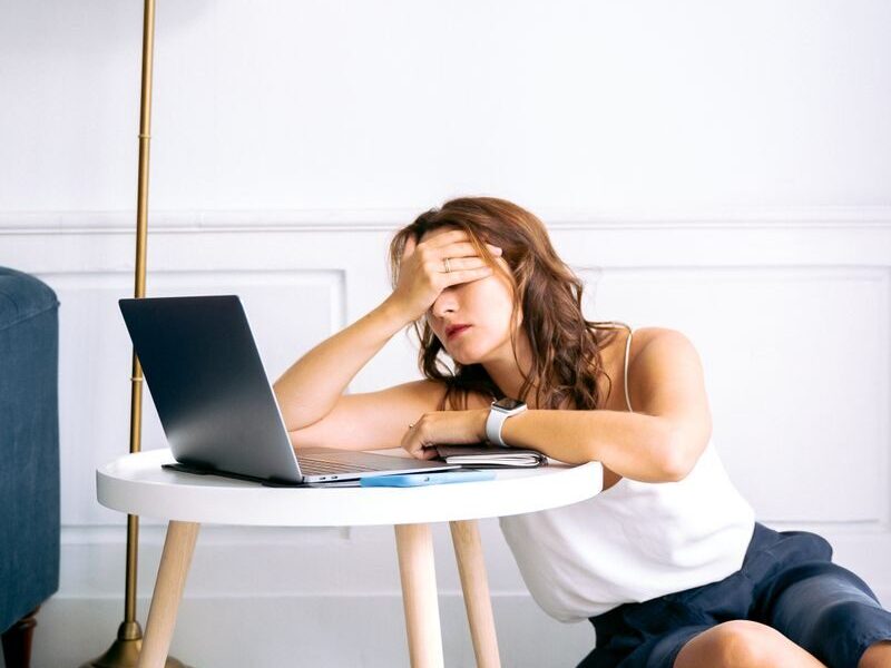 A woman showing signs of fatigue while working remotely at a laptop indoors.
