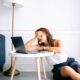 A woman showing signs of fatigue while working remotely at a laptop indoors.