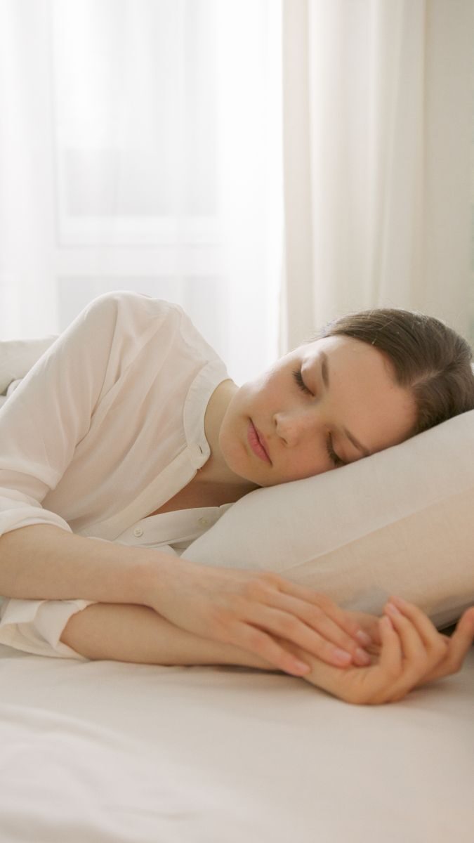 Calm woman sleeping in a white room, reflecting serenity and relaxation, ideal for lifestyle blogs.