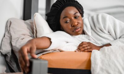 Woman in a cozy robe reaching for alarm clock in bedroom, waking up refreshed.