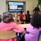 Students attentively watching a lesson on a smart board in a colorful Dutch classroom.