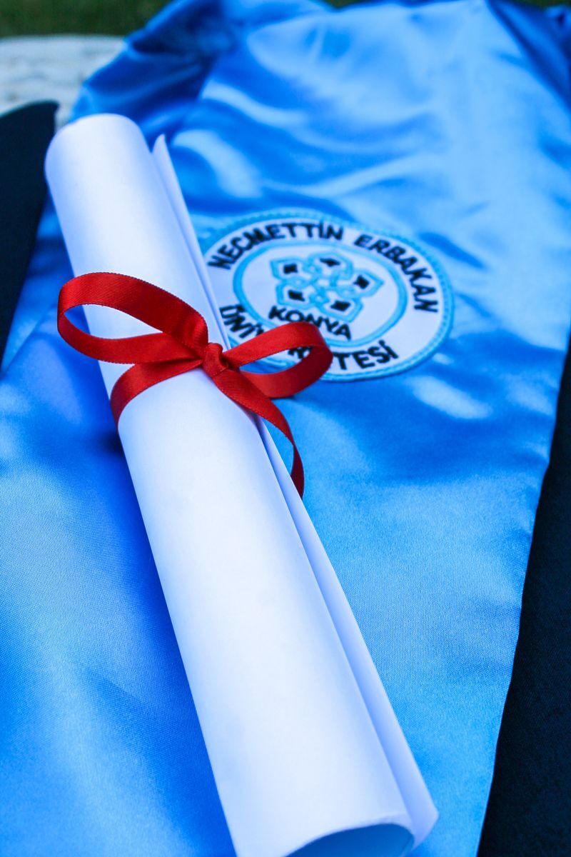 Rolled diploma with a red ribbon on a blue graduation gown, symbolizing academic achievement.