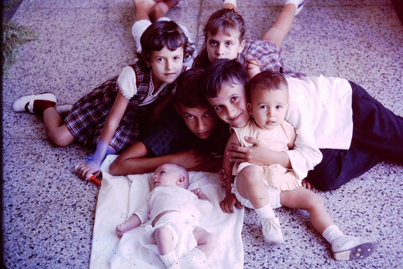 A heartwarming scene of siblings cuddled around a baby on a terrazzo floor.