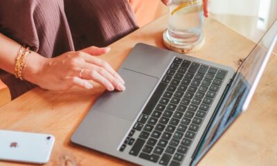 Woman using a laptop at home with a glass of lemon water, smartphone, and notebook on the table.
