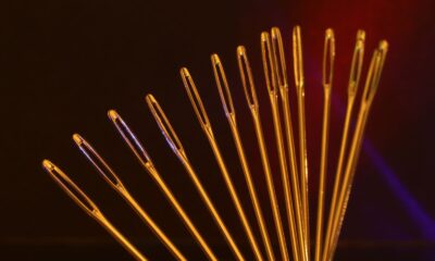 Artistic display of golden sewing needle eyes arranged in an arc against a dark backdrop.
