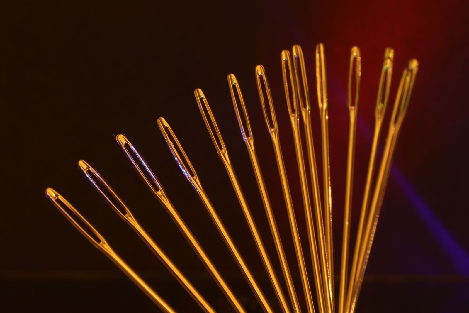 Artistic display of golden sewing needle eyes arranged in an arc against a dark backdrop.