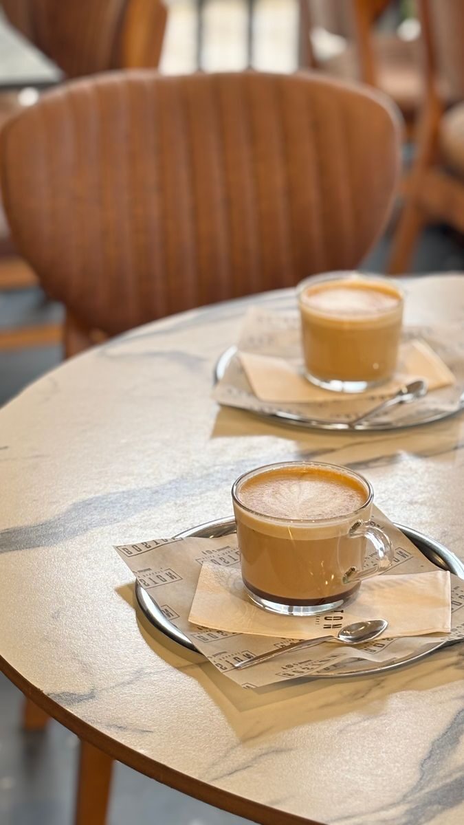 Two frothy cappuccinos on a marble cafe table, set for a cozy coffee break.