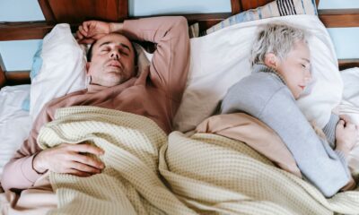 High angle of calm middle aged multiethnic couple in warm clothes lying and sleeping on soft bed in sunny morning
