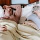 High angle of calm middle aged multiethnic couple in warm clothes lying and sleeping on soft bed in sunny morning