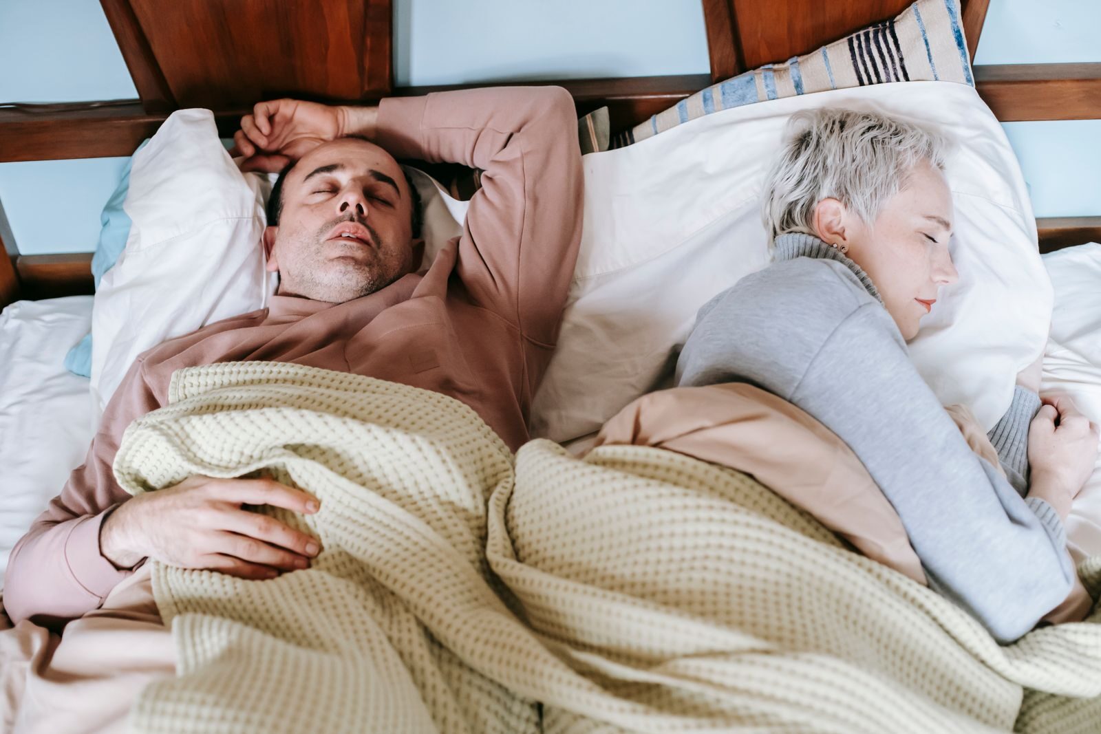High angle of calm middle aged multiethnic couple in warm clothes lying and sleeping on soft bed in sunny morning